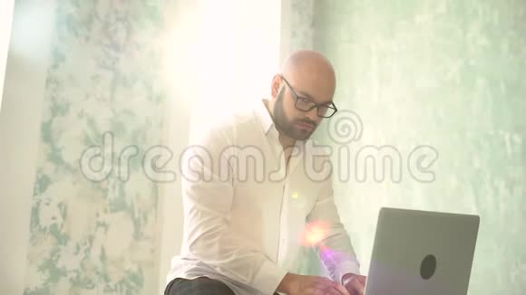 戴白眼镜的留胡子的人在室内使用笔记本电脑在笔记本电脑上工作的商人视频的预览图