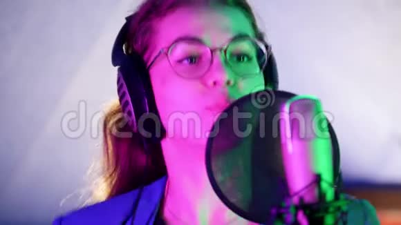 一个戴着耳机在录音室唱歌的年轻微笑的女人霓虹灯照明视频的预览图