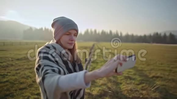 年轻女子在景观背景下的智能手机前摄像头上自拍视频的预览图