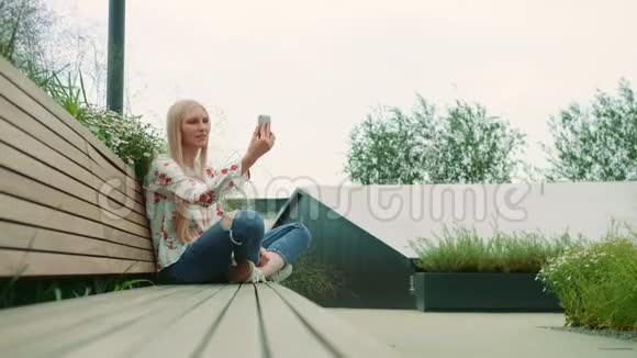 可爱的年轻女性使用智能手机做视频电话而坐在长凳上的巨大购物中心在美国视频的预览图