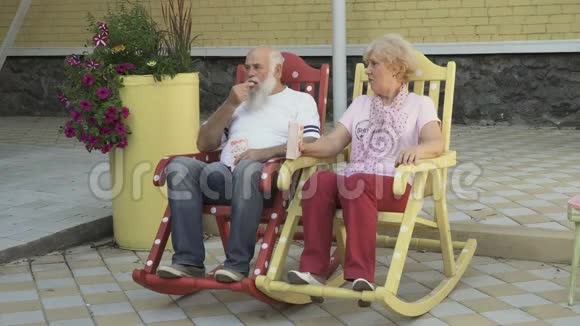 老人和老妇人在摇椅上休息吃爆米花视频的预览图