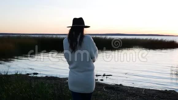 戴着帽子穿着白毛衣的女孩在日落散步视频的预览图
