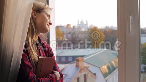一位美丽的年轻女子带着书望着窗外视频的预览图