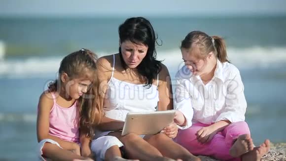 微笑的母亲和女儿在海滩上使用平板电脑视频的预览图