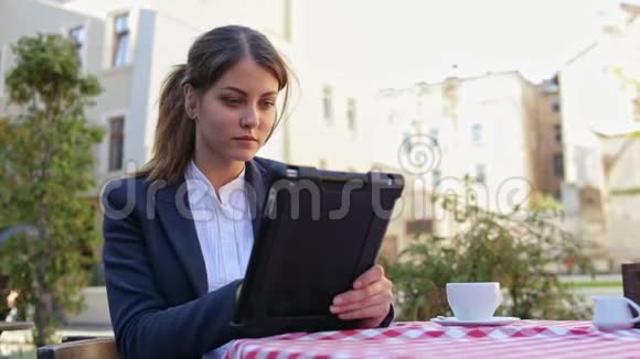 微笑可爱的年轻女人在咖啡馆的露台上用平板电脑喝咖啡视频的预览图