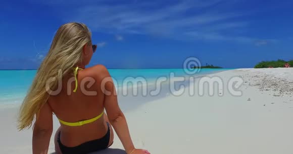 V09977美丽的年轻女孩穿着比基尼在阳光下的白色沙滩上享受蓝色海水的沐浴和放松视频的预览图