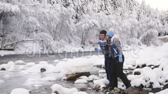 一个年轻幸福的家庭站在一条山河的河口恋爱中的情侣把鹅卵石扔进河里视频的预览图