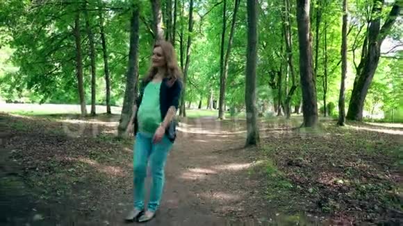 年轻的孕妇独自在公园散步抚摸她的腹部视频的预览图