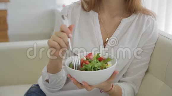 年轻女子在家里吃白碗里的希腊色拉视频的预览图