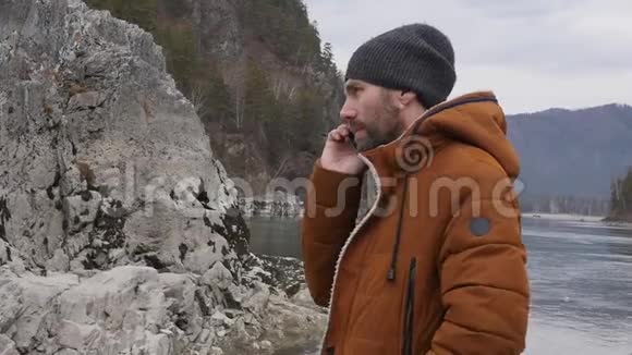大胡子的游客正在与朋友在一条山河畔的手机上举行视频会议慢动作视频的预览图