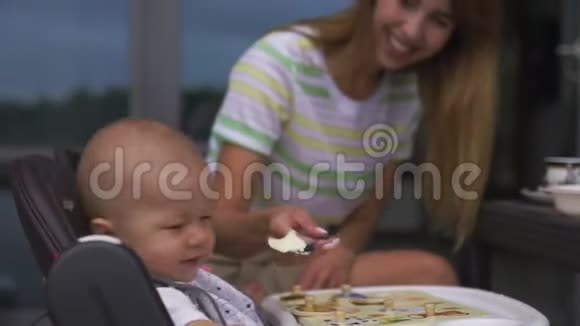 年轻的母亲喂养她的小儿子坐在孩子的座位上家庭价值观温暖的颜色夏天的场景视频的预览图