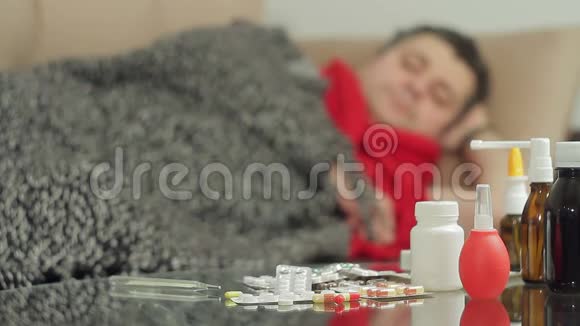 一个有感冒症状的男人躺在沙发上用毯子盖住房间测量房间的温度视频的预览图