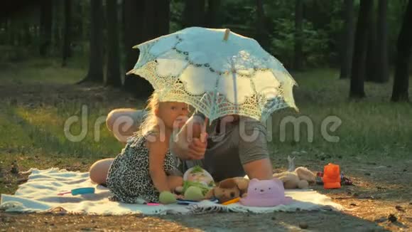 快乐的父亲和女儿在公园的毯子上放松从伞里窥视视频的预览图