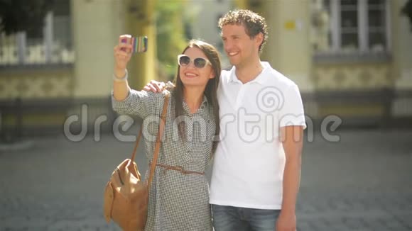 在阳光明媚的夏日年轻夫妇在城市广场上使用智能手机站立户外活动视频的预览图