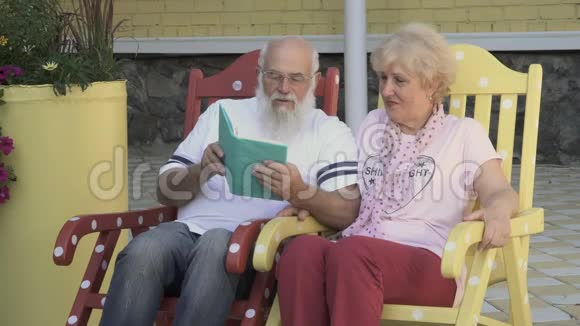 老人读一本书妻子亲吻她的脸颊在摇椅上放松视频的预览图