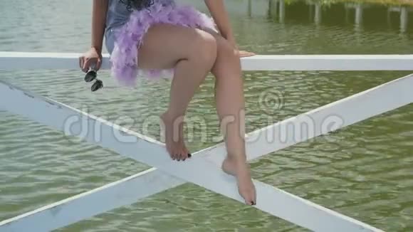 小女孩坐在河边的木栅栏上移动腿视频的预览图