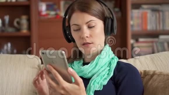 年轻女子在家用无线耳机听音乐唱歌敲智能手机屏幕视频的预览图