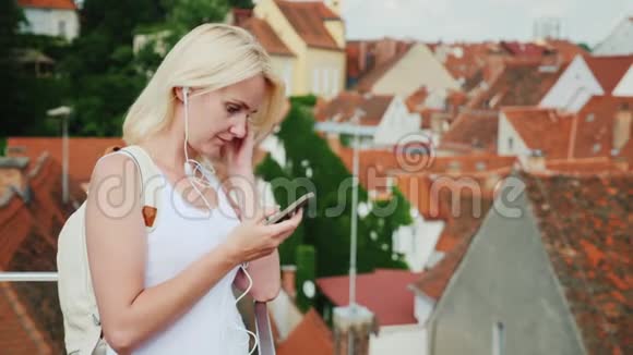 带智能手机和耳机的年轻女人享受奥地利格拉茨市的老城区反对视频的预览图