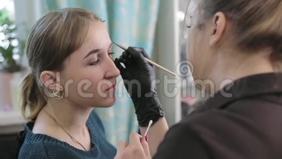 化妆师和模特一个女人的特写她漂亮的脸化妆师给一个漂亮女孩画眉毛视频的预览图