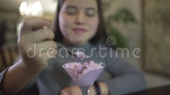 在咖啡馆里用银勺吃紫罗兰色冰淇淋的胖嘟嘟的黑发小少女近距离观看视频的预览图