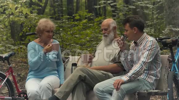 年长的女人和男人和年轻人在公园的长凳上喝茶视频的预览图
