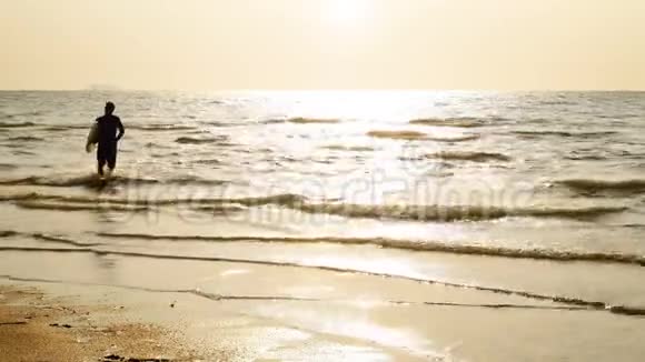 4K在热带海滩日落时年轻快乐的冲浪男子带着长长的冲浪板跑步的剪影海边的冲浪者视频的预览图