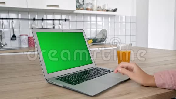 迷人的年轻女性使用笔记本电脑在现代厨房吃苹果女性看着电脑屏幕咬着绿色的绿色视频的预览图