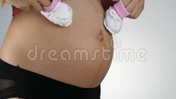 穿着内衣的孕妇在肚子上玩婴儿鞋慢动作视频的预览图