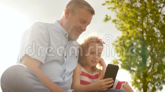 祖父和孙女看智能手机可爱的女孩和成熟的男人玩手机视频的预览图