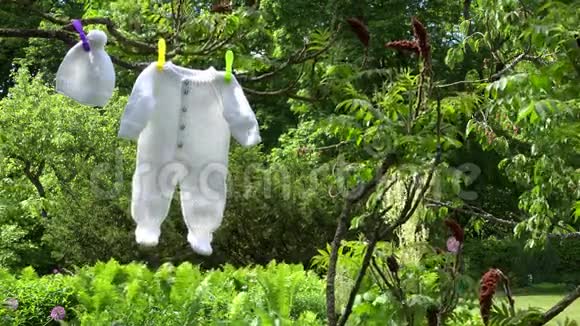 白色婴儿衣服身体和帽子挂在花园的树枝上视频的预览图