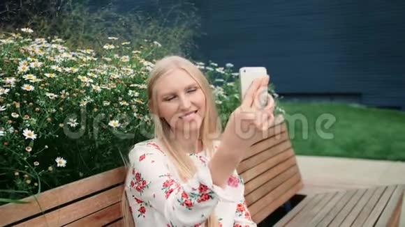 可爱的年轻女性使用智能手机打视频电话而坐在长凳上的生活屋顶的巨大购物中心视频的预览图