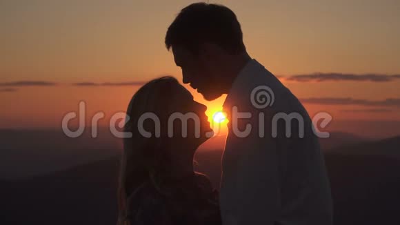 英俊的男人在夕阳的背景下亲吻他的情人的额头和嘴唇视频的预览图