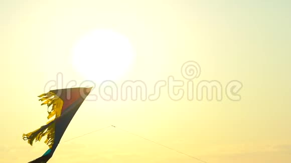 特写玩具风筝在风中高高飘扬映衬金色晚霞天空背景太阳镜头耀斑五颜六色的风筝飞进来视频的预览图