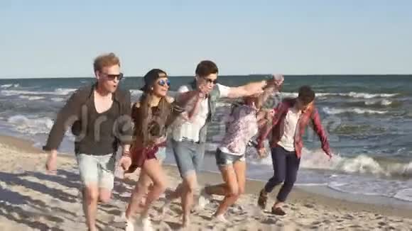 一群年轻的嬉皮士朋友一起跑手牵着手在海边水边慢镜头视频的预览图