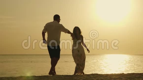 一对年轻夫妇的剪影在大海和夕阳的背景下滑稽地跳舞假期愉快视频的预览图
