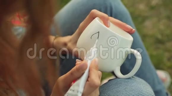 女孩的手白色杯子上画了一个图案女孩在晚上坐在草地上画装饰品视频的预览图