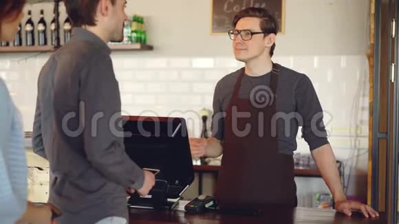 友好的咖啡师帅哥卖外卖咖啡用智能手机接受非接触式移动支付视频的预览图
