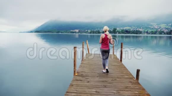 一个木墩上的年轻女子他欣赏风景奥地利阿尔卑斯山的山湖视频的预览图
