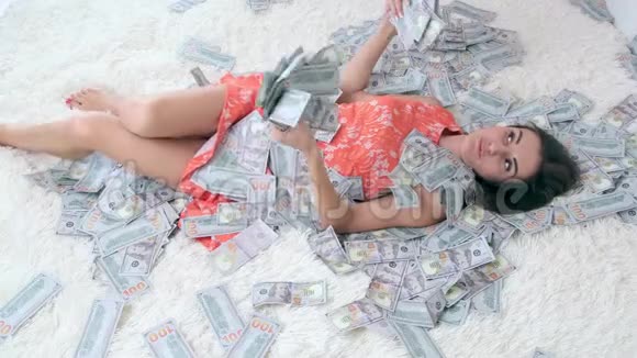 在一张白色的床上和一个漂亮的女孩有很多钱巨大财富的概念视频的预览图