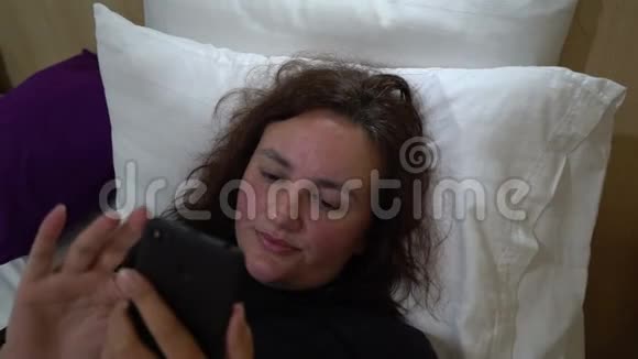 年轻漂亮的女人在床上使用拿着智能手机疲倦困倦不快乐视频的预览图