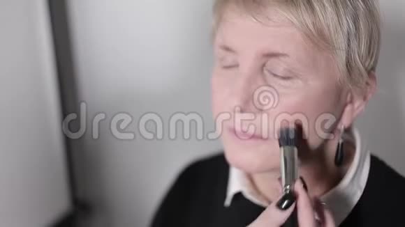 化妆师做化妆的中年女人年龄化妆特写肖像用刷子涂抹粉末视频的预览图
