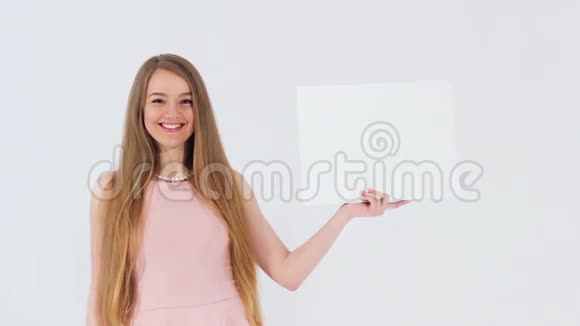 微笑迷人的女孩穿着粉红色的裙子靠近看着相机拿着一个白色的空白横幅视频的预览图