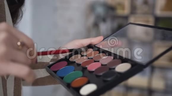 特写镜头一个调色板与眼影和化妆师手的化妆刷女孩拿着五颜六色的调色板视频的预览图