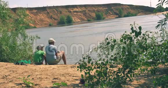 快乐父子正坐在河岸上钓鱼爸爸和儿子正在早上钓鱼家庭幸福视频的预览图