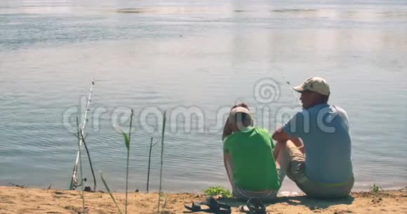 一对幸福的父子坐在河岸上钓鱼爸爸和儿子早上在钓鱼一个幸福的家庭视频的预览图