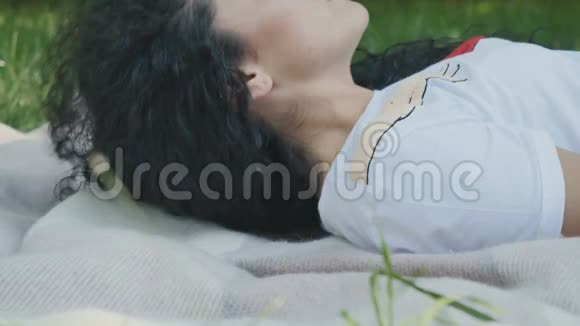 美丽的黑发姑娘躺在公园的格子布上微笑着视频的预览图