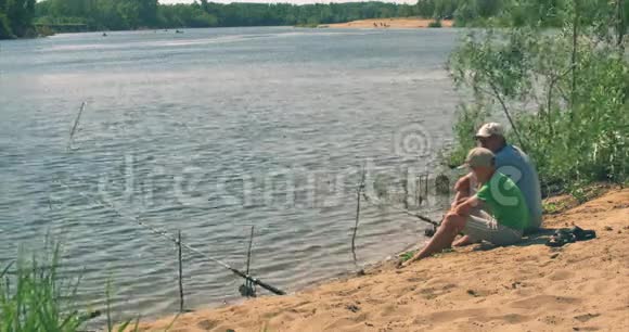 快乐父子正坐在河岸上钓鱼爸爸和儿子正在早上钓鱼家庭幸福视频的预览图