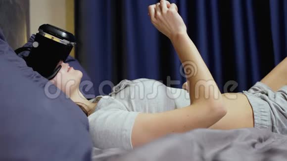 躺在床上枕头上的年轻女性使用虚拟现实观看VR视频视频的预览图