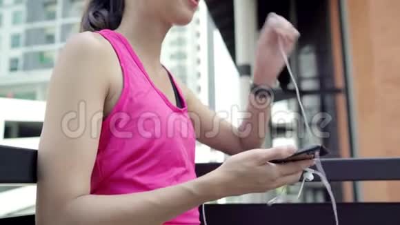 健康美丽的年轻亚洲运动员妇女使用智能手机听音乐同时在城市跑步视频的预览图