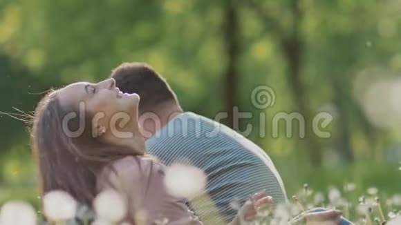 一对浪漫的情侣在夏天的白蒲公英的空地上他们高兴地吹着蒲公英他们掉进了视频的预览图
